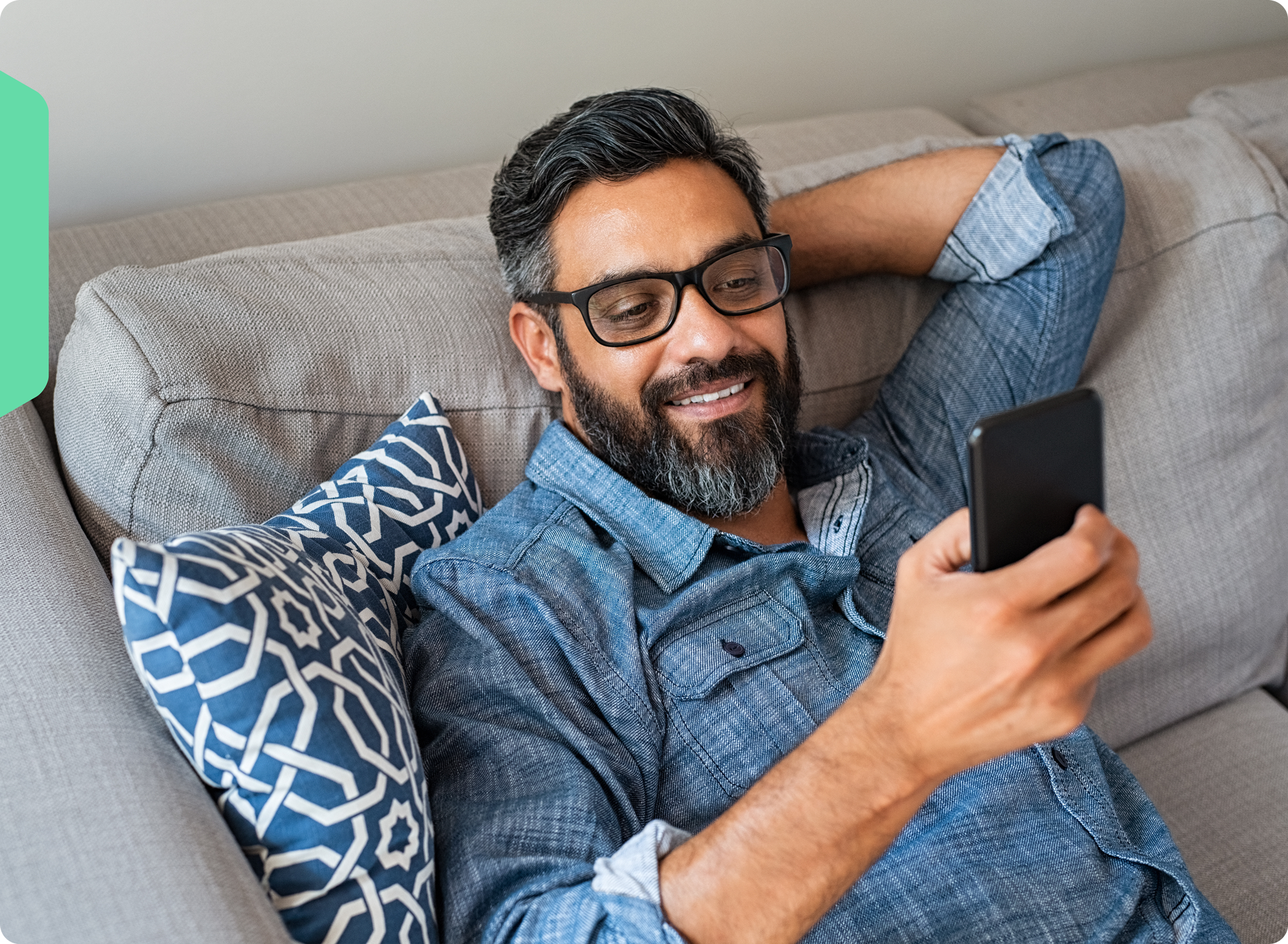 A man, smiling, browsing Wholescripts.com on his phone from his couch