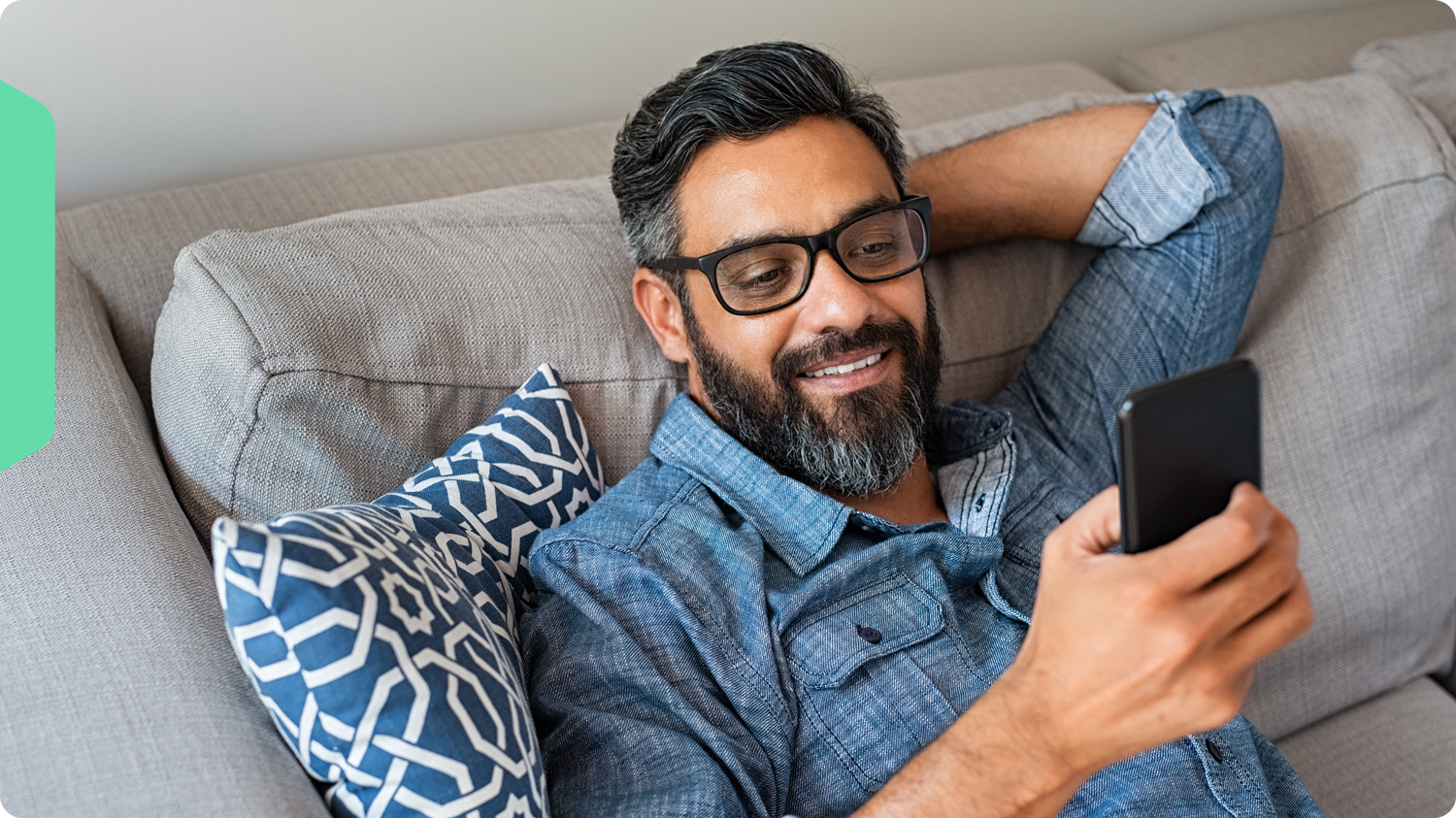 A man, smiling, browsing Wholescripts.com on his phone from his couch